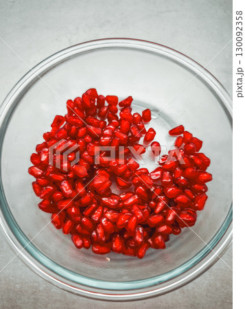 Fresh pomegranate seeds filling a glass bowl on a table 130092358