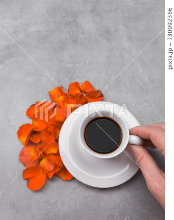 Hand holding coffee cup near orange petals on gray background Hand holding coffee cup near orange petals on gray background 130092386