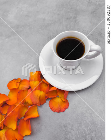 White cup of coffee with orange rose petals on gray background 130092387