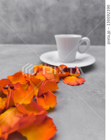Orange rose petals leading to a white coffee cup on a gray table Orange rose petals leading to a white coffee cup on a gray table 130092390
