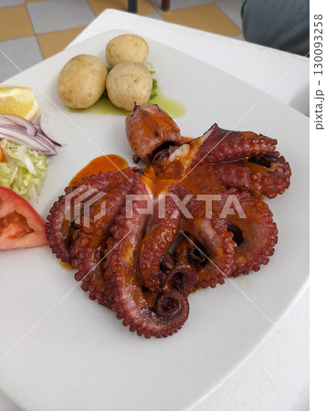 Delicious grilled octopus served with potatoes, salad, and lemon on a white plate, a flavorful dish. 130093258