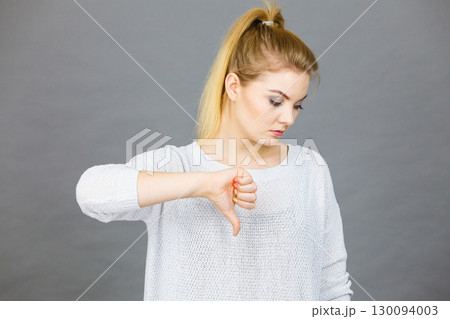 Sad woman showing thumb down gesture 130094003
