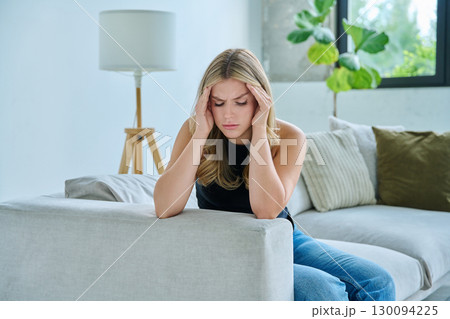 Unhappy upset young woman having headache, sitting on sofa at home 130094225