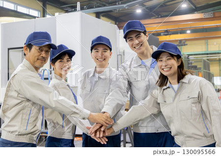 工場の中で円陣を組む作業員グループ 130095566