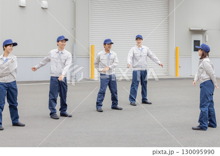 工場の前で体操する作業員グループ 130095990