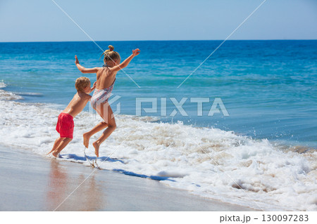 Happy kids have fun in sea surf on white sand beach. Couple of children sit in water pool. Travel lifestyle, swimming activities in family summer camp. Vacations on tropical island. 130097283