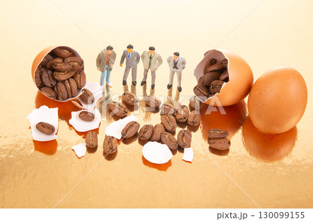 Miniature figures in business and casual attire gather around cracked orange eggs  130099155
