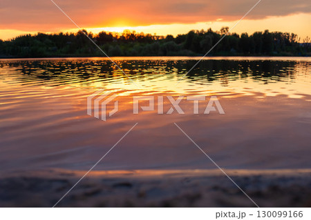 Stunning sunset over a peaceful lake, reflecting vibrant orange hues on rippling water 130099166