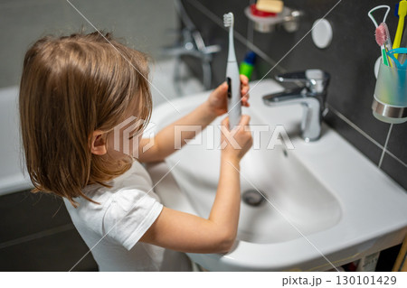 Little girl brushing her teeth with an electric toothbrush in the bathroom in the morning. Concept of personal hygiene and daily morning routine in childhood. 130101429
