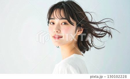 柔らかな風に髪が揺れるスタジオで微笑む若い女性 130102228