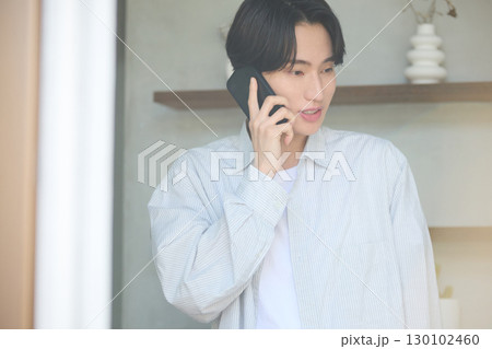 窓際で電話をしている若いアジアの男性 130102460