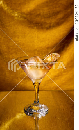 Golden cocktail with ice cube and dried citrus slice on reflective background 130104170