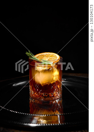 Old fashioned cocktail with orange slice and rosemary on reflective black tray 130104173