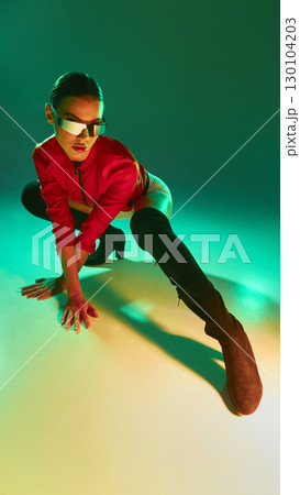 Dynamic woman in red jacket and futuristic shades crouching with dramatic green lighting 130104203