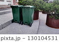 Two green trash bins placed beside large planters in a clean urban setting 130104531