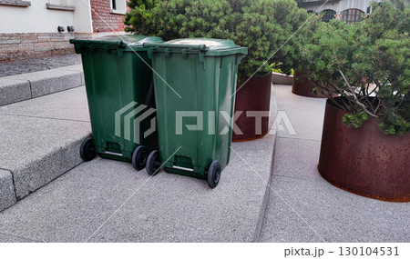 Two green trash bins placed beside large planters in a clean urban setting Two green trash bins placed beside large planters in a clean urban setting 130104531