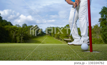 Golfer putting ball on the green golf, lens flare on sun set evening time. Golfer hitting golf ball. 130104762