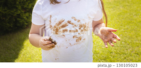 Girl child staining her white t-shirt with stain while enjoying a delicious chocolate bar in garden 130105023