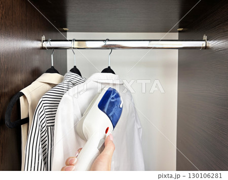 Woman ironing clothes with steam iron at wardrobe. Clothes care and garment steaming. Fashion, laundry, household chores, wrinkle removal. Business and casual clothing care Woman ironing clothes with steam iron at wardrobe. Clothes care and garment steaming. Fashion, laundry, household chores, wrinkle removal. Business and casual clothing care 130106281