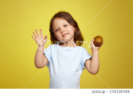 funny little child girl holding kiwi fruit on yellow background 130106388