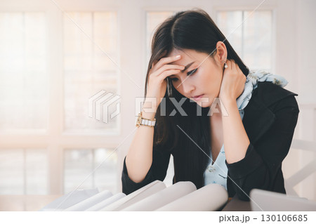 Young asian woman architect holding forehead and neck while working on project at office desk. She is tired and tired. Young asian woman architect holding forehead and neck while working on project at office desk. She is tired and tired. 130106685