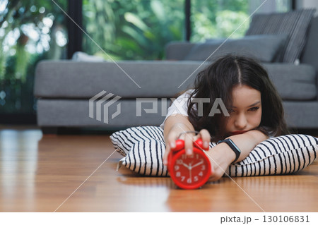 Young asian woman reaching over to turning off alarm clock while lying on the floor in living room at home. 130106831