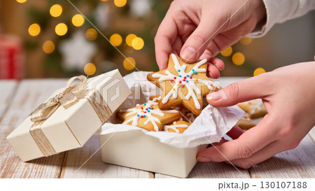 Christmas star-shaped cookies with icing and sprinkles in a gift box held by hands, festive background with warm holiday lights 130107188