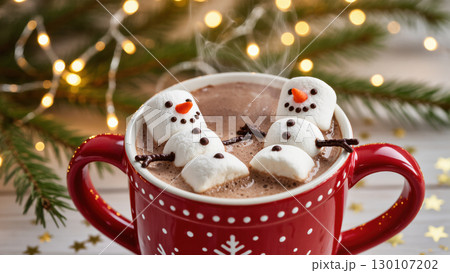 Christmas hot chocolate with marshmallow snowmen in red mug, festive lights and fir branches in warm holiday setting Christmas hot chocolate with marshmallow snowmen in red mug, festive lights and fir branches in warm holiday setting 130107202
