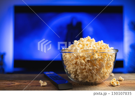 A glass bowl of popcorn and remote control in the background the TV works A glass bowl of popcorn and remote control in the background the TV works 130107835