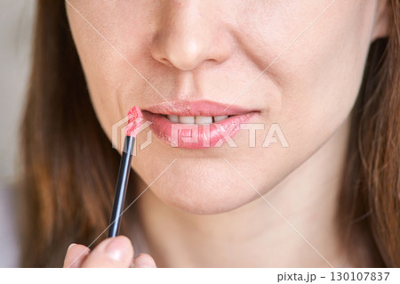 Young caucasian female applying pink lipstick close up with lip brush for beauty Young caucasian female applying pink lipstick close up with lip brush for beauty 130107837