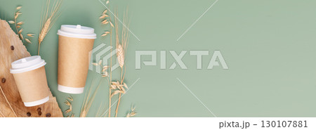 Healthy coffee substitutes banner. Eco decaf coffee made from barley and wheat. Two disposable eco-friendly cardboard cups with wheat and rye ears, coffee beans on green background. Takeaway coffee 130107881