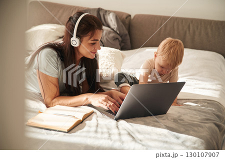 On the comfortable bed. Mother with her little son is at home in domestic room 130107907