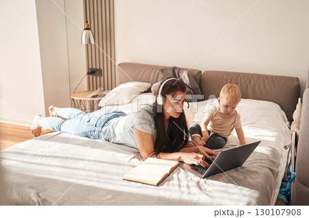On the comfortable bed. Mother with her little son is at home in domestic room On the comfortable bed. Mother with her little son is at home in domestic room 130107908
