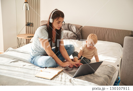 Showing laptop. Mother with her little son is at home in domestic room Showing laptop. Mother with her little son is at home in domestic room 130107911