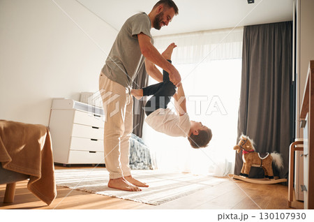 Playing, holding in hands. Man is playing with his little son in the domestic room 130107930