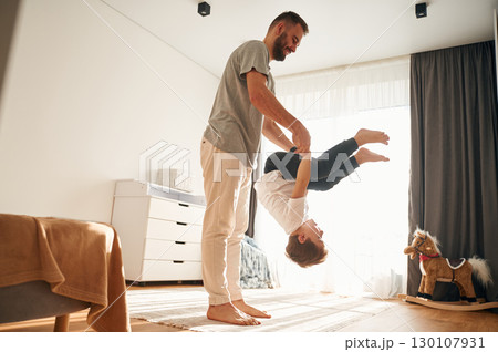 Holding kid upside down. Man is playing with his little son in the domestic room 130107931