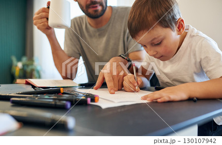 Writing the homework. Father and son are at home by the table 130107942