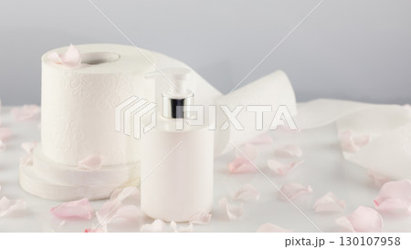 Roll of toilet paper with cosmetic dispenser bottle on light background with rose petals and copy space. White toilet tissue, Hygiene product. Restroom soft touch toilet paper. Soft focus style image Roll of toilet paper with cosmetic dispenser bottle on light background with rose petals and copy space. White toilet tissue, Hygiene product. Restroom soft touch toilet paper. Soft focus style image 130107958