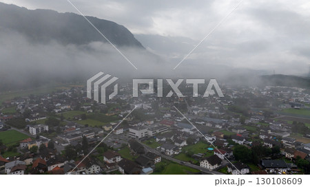 Aerial view of Haiming, Tyrol, Austria, on a cloudy morning with low lying fog partially covering the town and surrounding mountain landscape Aerial view of Haiming, Tyrol, Austria, on a cloudy morning with low lying fog partially covering the town and surrounding mountain landscape 130108609