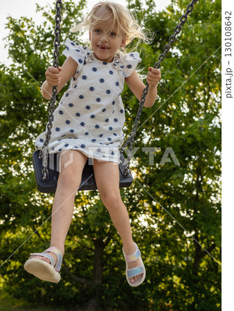 Carefree girl enjoying a playful moment swinging on a swing set in a park during summer holidays, childhood memories and outdoor recreation 130108642