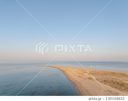 Breathtaking aerial view of a sailboat moored near a beautiful sandy spit in Khalkidhiki, Greece, as the sun rises, creating a serene and idyllic scene 130108652