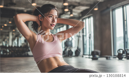 女性がジムで汗を流し腹筋運動に励む姿 130108814