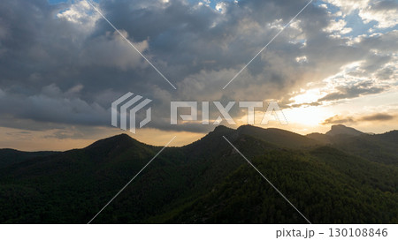 Sunbeams are filtering through a cloudy sky at sunset, illuminating the peaks of the mountains in Gilet, Spain 130108846
