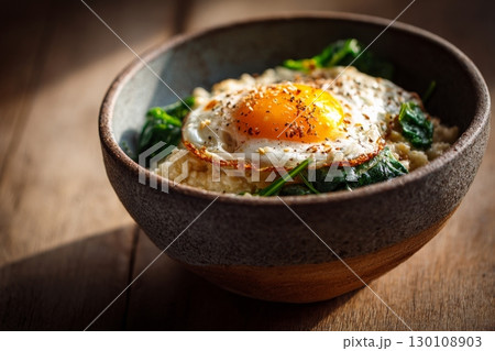 A bowl of creamy oatmeal topped with a fried egg and cooked spinach on a wooden table, in warm sunlight. Healthy breakfast concept A bowl of creamy oatmeal topped with a fried egg and cooked spinach on a wooden table, in warm sunlight. Healthy breakfast concept 130108903