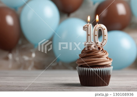 A chocolate cupcake with '10' candles against blue and brown balloons. 130108936