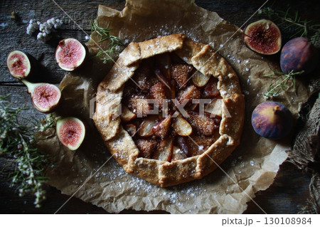 A rustic galette with fresh figs and herbs on parchment paper. 130108984
