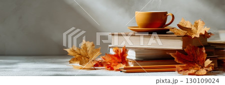 A cozy autumn scene with a warm mug and pencils in a holder on top of stacked books, surrounded by orange and brown autumn leaves. Back to scgool banner 130109024