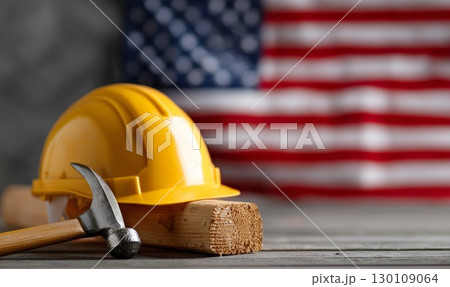 A yellow construction helmet and hammer on wooden block with American flag in background. Labor Day holiday in USA 130109064