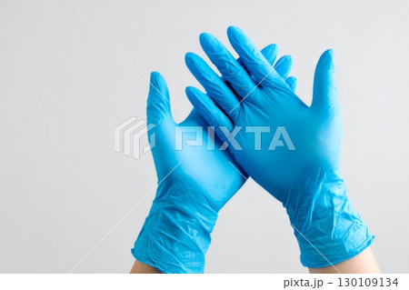 Two hands wearing blue latex gloves held up against a light gray background. 130109134