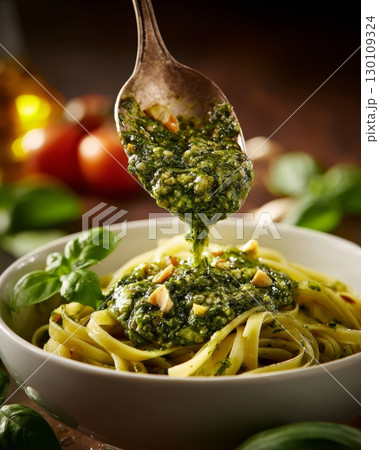 A delicious bowl of pasta topped with fresh green pesto being drizzled from a spoon. 130109324
